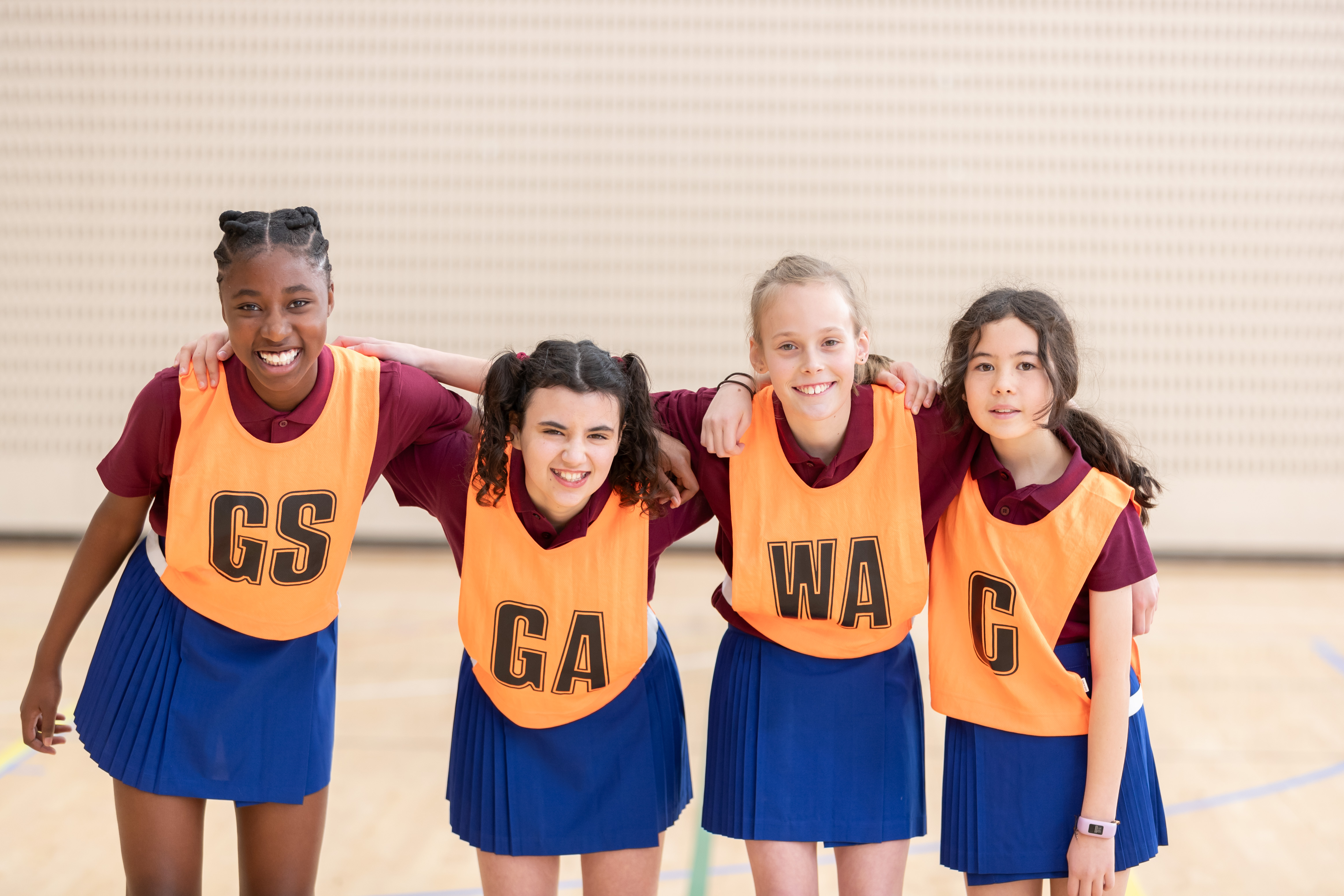 Image of four girls wearing netball bibs smiling at the camera.
