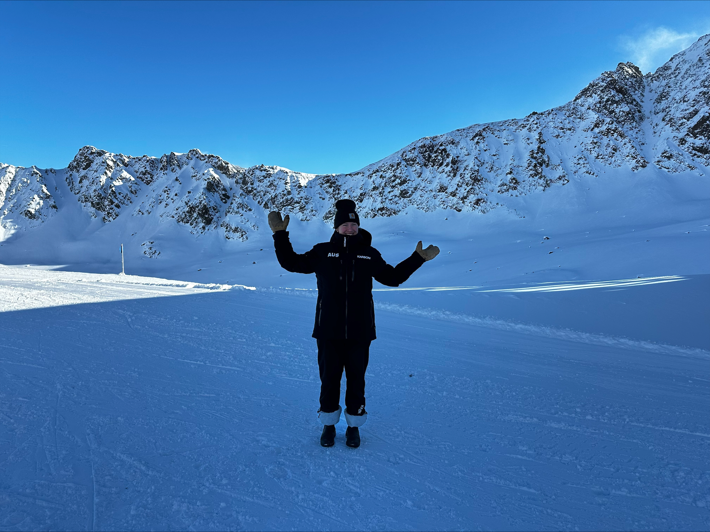 Amelia Hodgson standing in the snow in front of a mountain range with arms outstretched