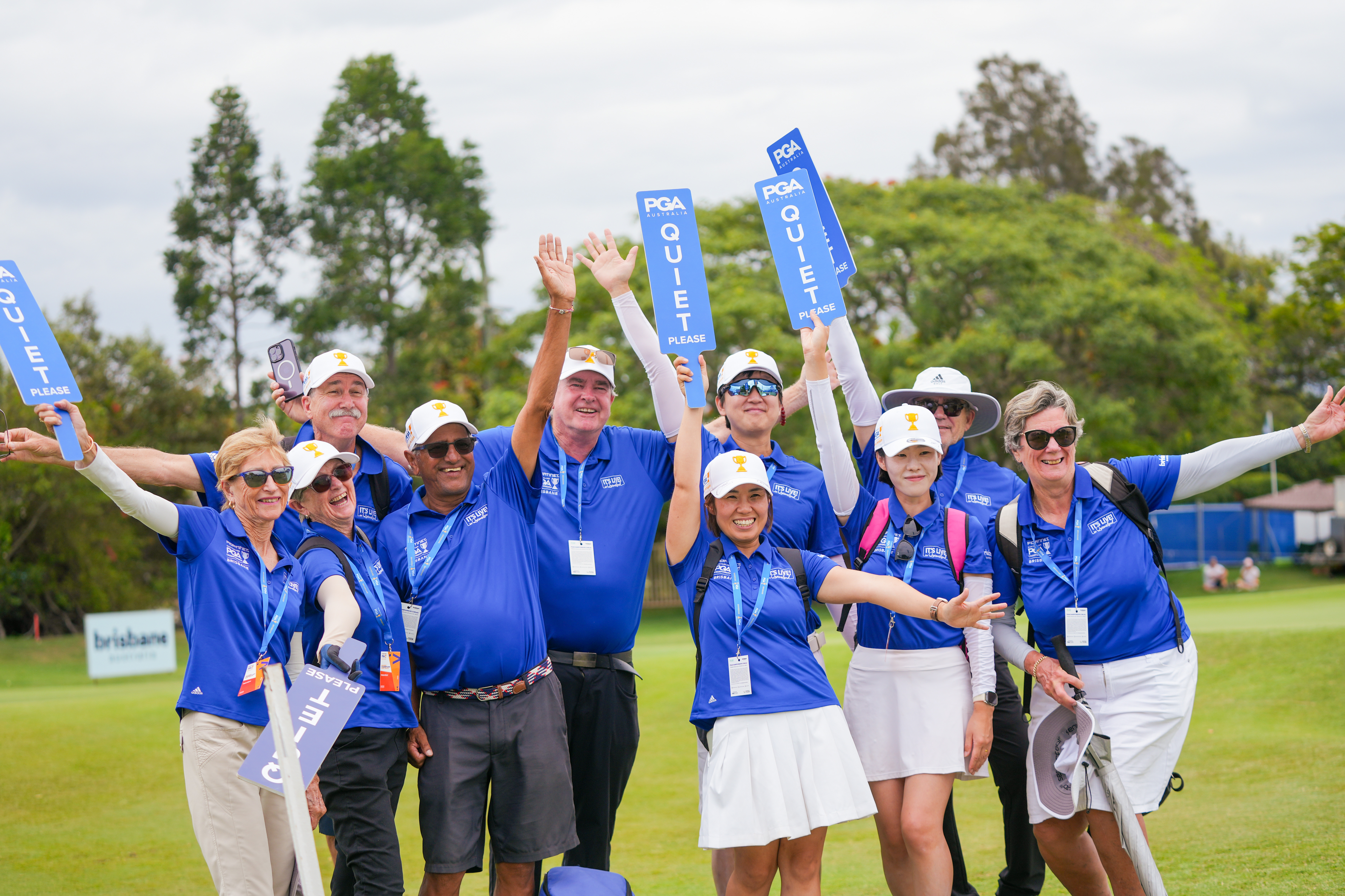 10 volunteers dressed in blue shirts working at the 2023 Australian PGA Championship in Queensland holding 'Quiet Please' signs