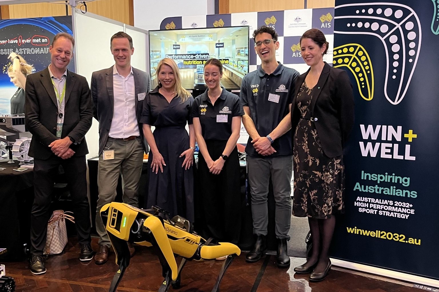 Six members of the Australian Sports Commission standing in front of their booth at the Government Scientists Group STEM Expo held at Parliament House 