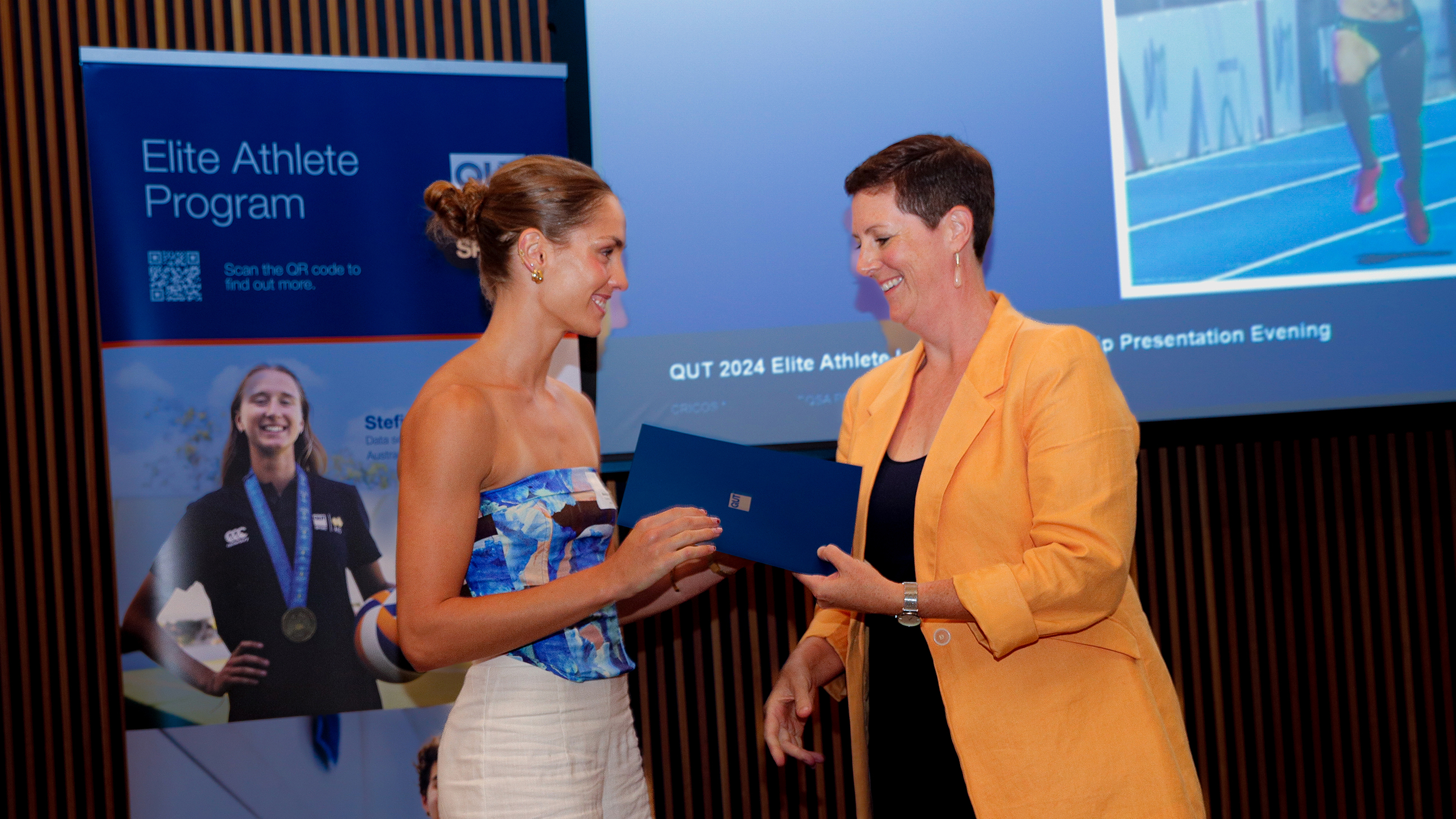 Runner Monique Hanlon recieves an envelope from the AIS National Wellbeing Manager Sonia Boland on stage at the QUT Elite Athlete Program presentation evening