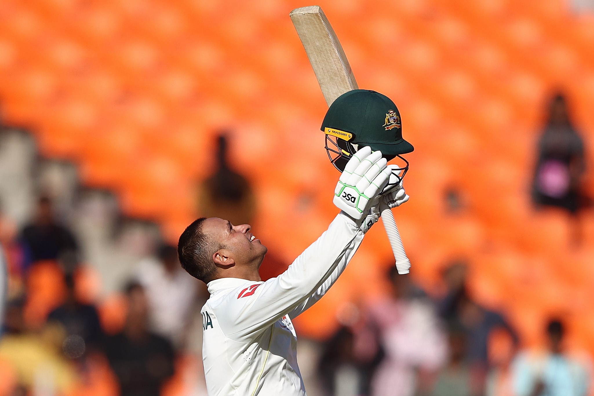 Usman Khawaja raises bat and helmet.