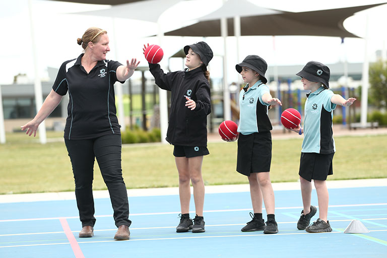 Image of a teacher showing children how to bowl as part of a Sporting Schools cricket program.